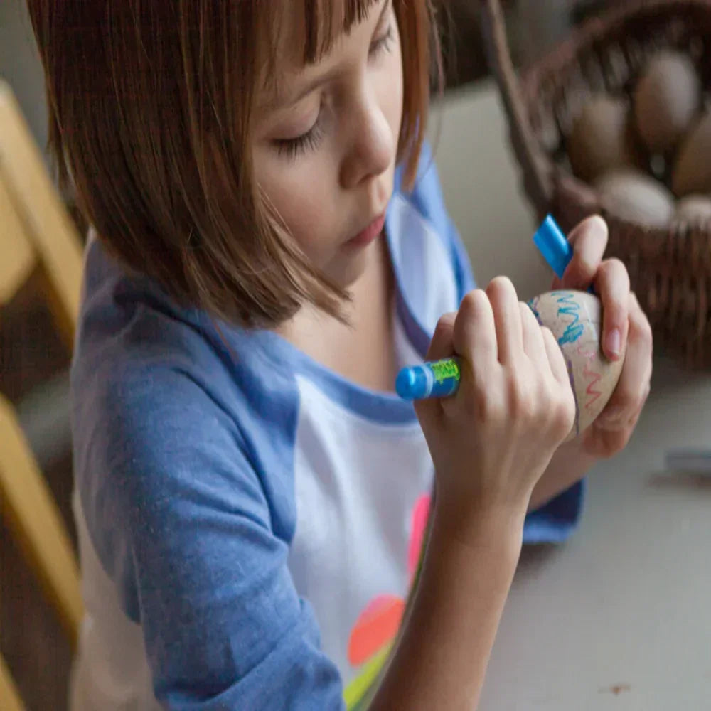 Child drawing colorful designs on an egg with a blue art marker for crafts