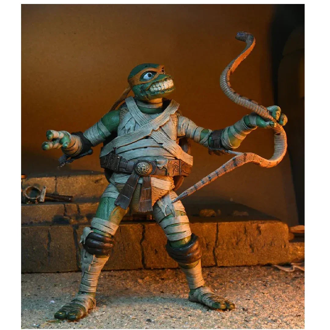 Action figure of a ninja turtle in bandages holding nunchucks, posed in a diorama setting.