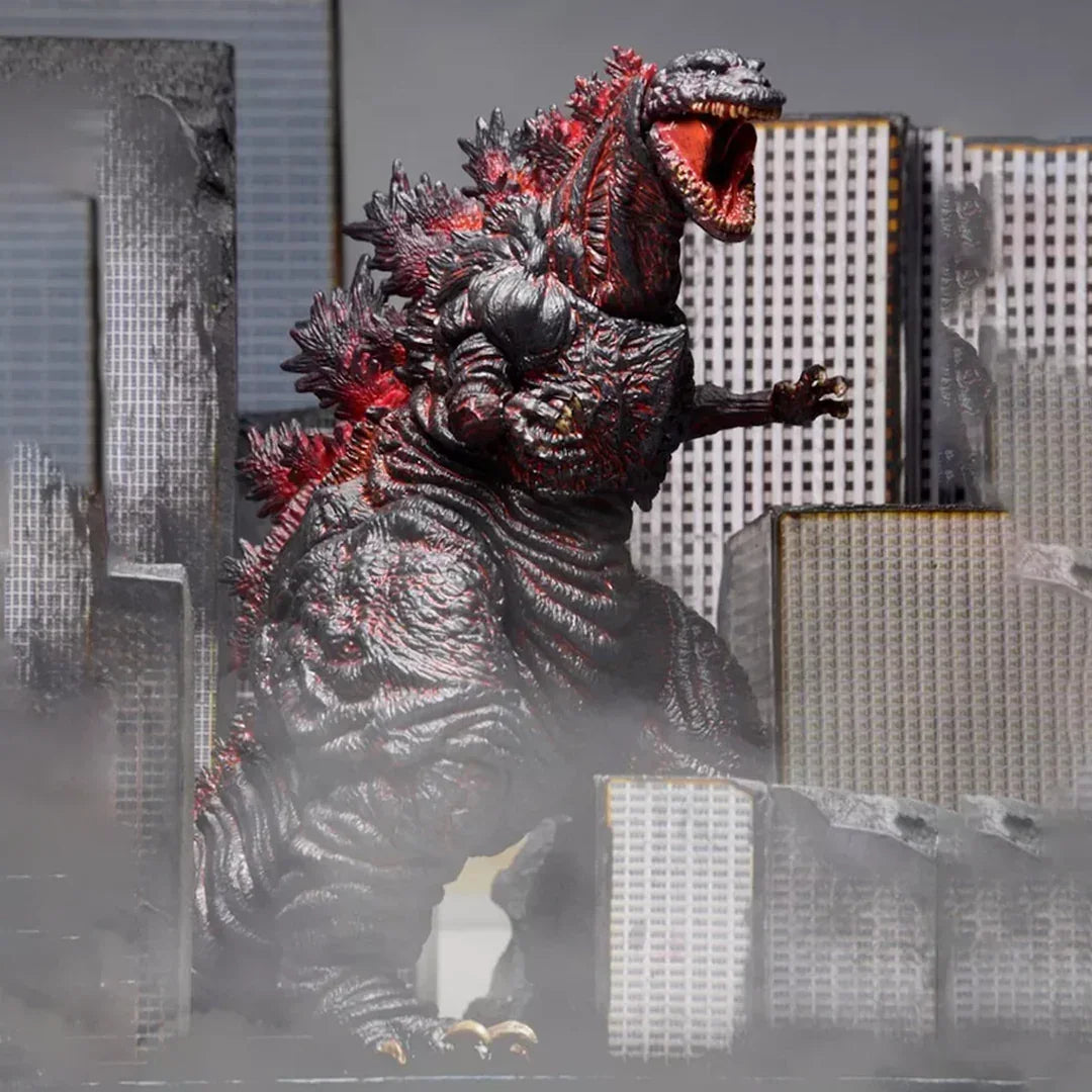 Godzilla action figure toy posed among destroyed city buildings with smoky background
