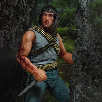 Action figure holding a knife in a forest setting, wearing ammo belts and a headband