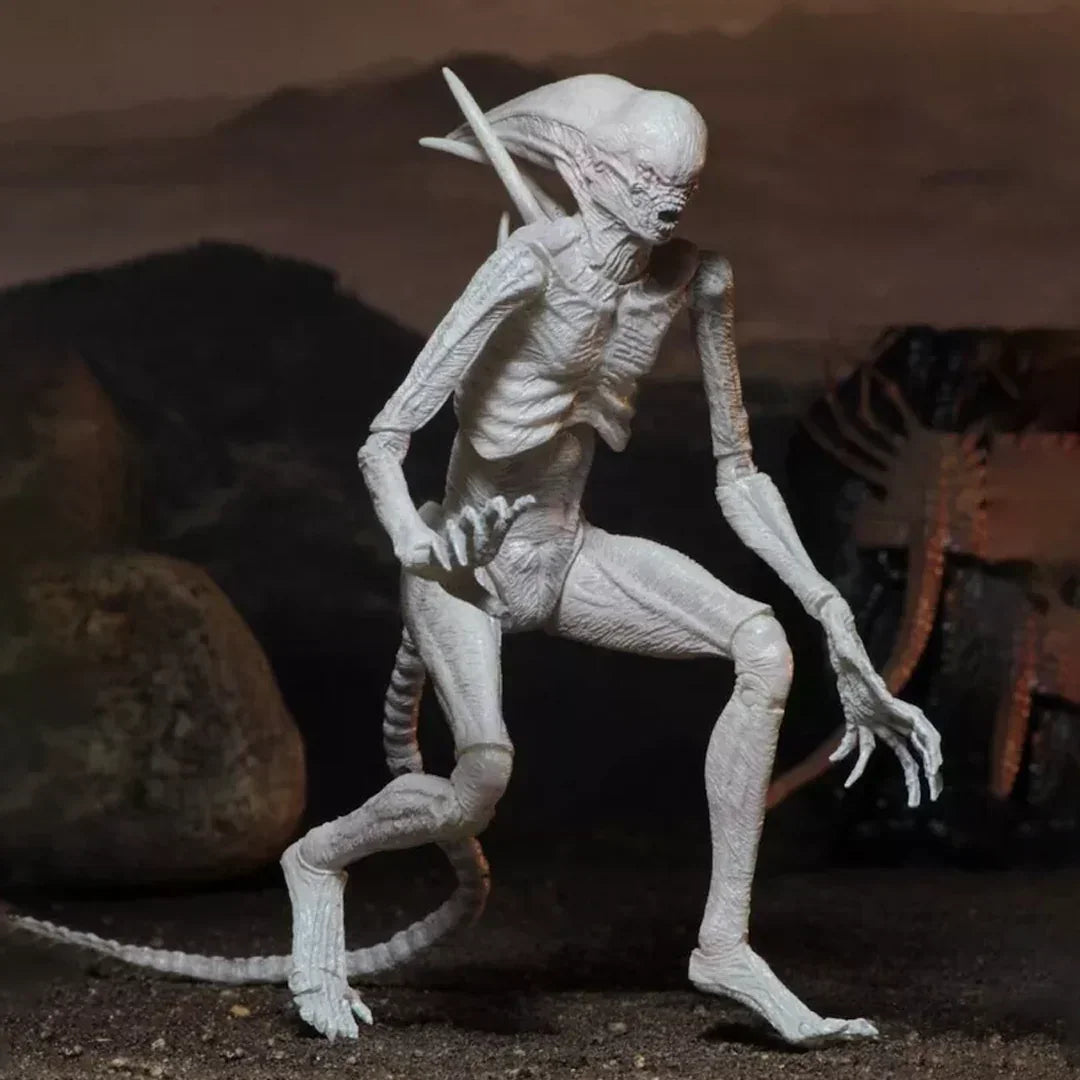 White alien creature action figure with elongated limbs and tail posed on rocky terrain