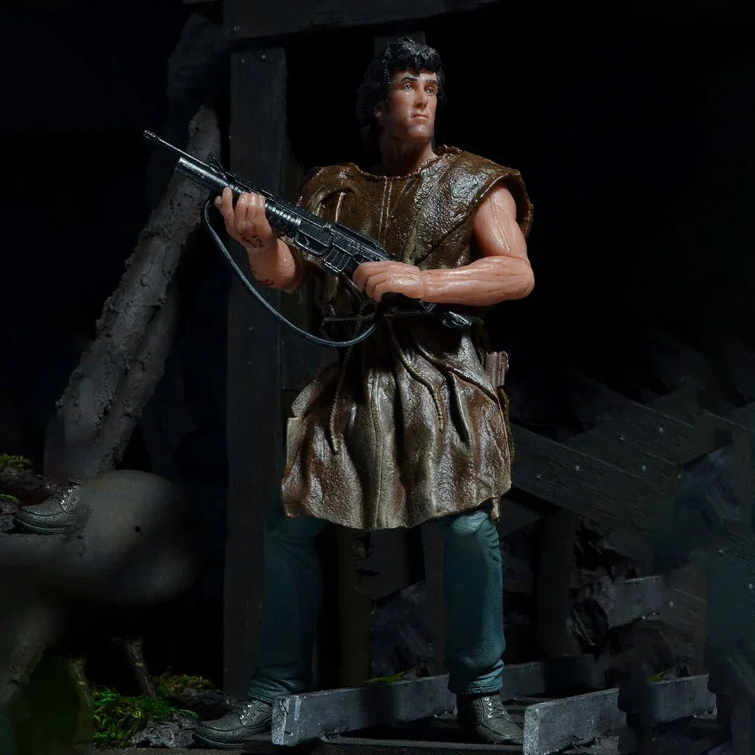 Action figure of a muscular man in outdoor gear holding a rifle in a rugged, dark setting.