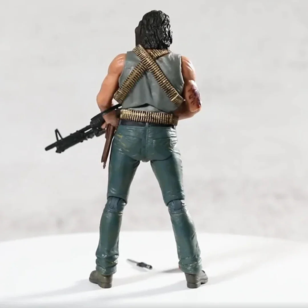Action figure with black hair, green pants, ammo belts, and a rifle, viewed from behind.